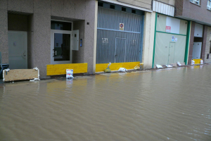 Eine überflutete Straße mit Wasser bis zum Fenster- und Türiveau, das die Umgebung und Gegenstände unterspült.