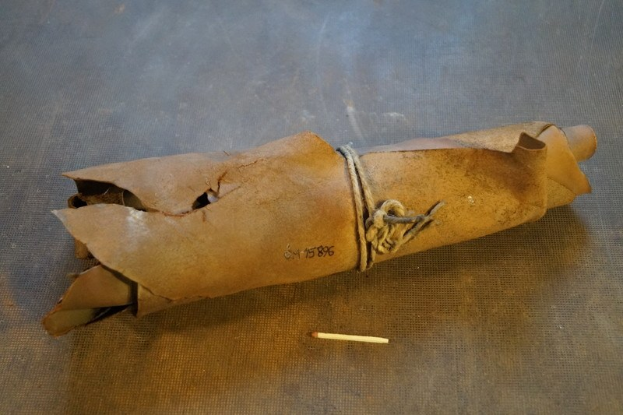 Ein brauner Papiertüte in Form einer Granate, mit einem Seil verschnürt, liegt auf einem Tisch neben einer Zigarette.