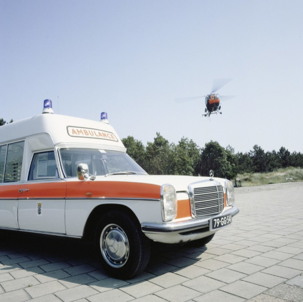 Ambulanz vor einem Hubschrauber mit Bäumen und einem klaren blauen Himmel im Hintergrund geparkt.