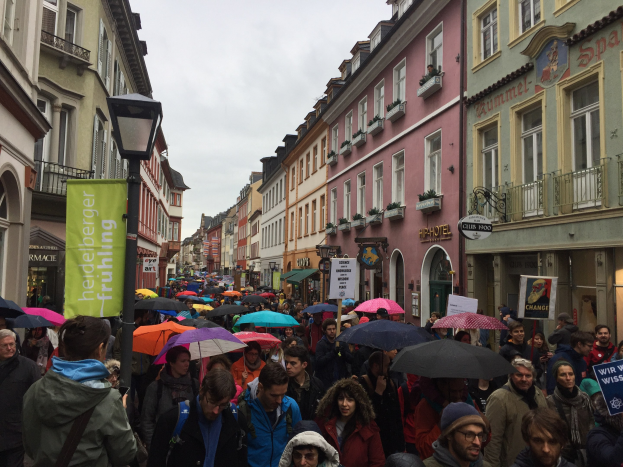 Eine große Gruppe von Menschen geht auf einer Straße mit Schirmen, einige tragen Taschen und halten Schilder, während sie an einer Klimademonstration in Deutschland teilnehmen.