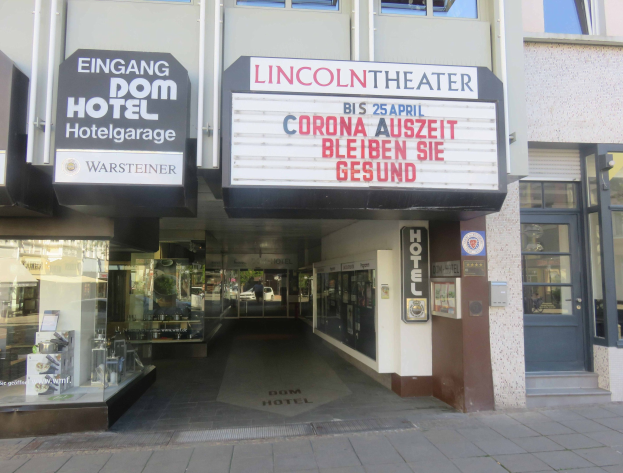 Außenansicht des Lincoln Theaters in Berlin, Deutschland, mit Glasfenstern und -türen sowie einer Tafel und einem Innenraum, der eine pulsierende Stadtkulisse suggeriert.
