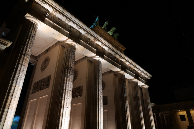 Das Brandenburger Tor in Berlin nachts, beleuchtet von Stadtlichtern, mit Skulpturen und Säulen gegen den Nachthimmel.