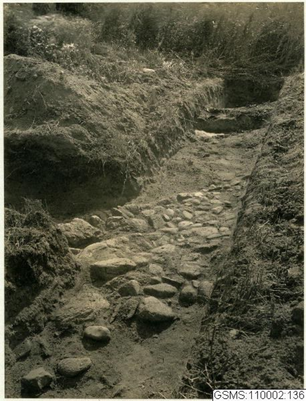 Schwarz-weiß-Foto eines Schotterwegs, der sich durch ein grasbewachsenes Feld schlängelt, mit Steinen auf beiden Seiten und einem Text am unteren Rand, der 'Der Weg nach oben' lautet.
