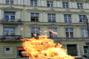 Ein großes Feuer brennt vor einem Gebäude mit Fenstern, Türen, einem Laternenmast und einer Tafel.