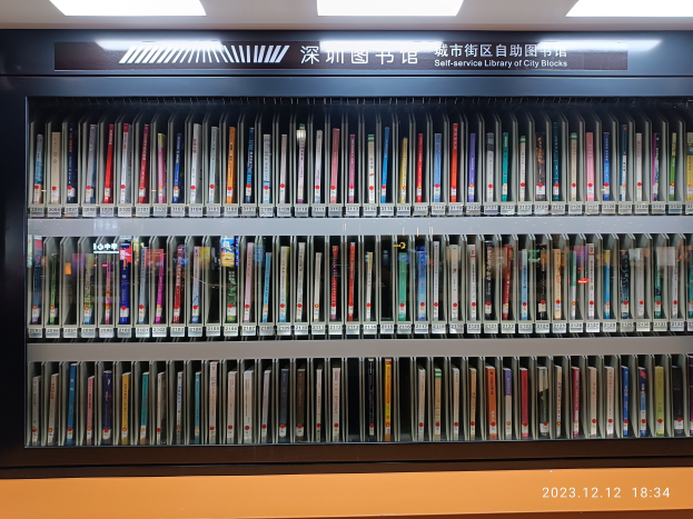 Eine gut beleuchtete Bibliothek mit hohen Bücherregalen, gefüllt mit Büchern, einer sichtbaren Texttafel und einem Wasserzeichen unten, das eine Selbstbedienungsstadtbibliothek suggeriert.