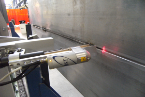 Eine Laser-Schneidmaschine in einer Fabrik strahlt helles Licht aus und erleuchtet die umliegende Fläche mit einer Wand auf der rechten Seite und einigen Gegenständen im Hintergrund.