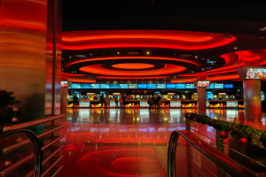 Ein Casino-Innenraum mit einem Weihnachtsbaum in der Mitte, gefliestem Boden, Geländern auf beiden Seiten, dekorierten Säulen und Deckenlampen, mit Menschen im Hintergrund, die eine festliche Atmosphäre schaffen.