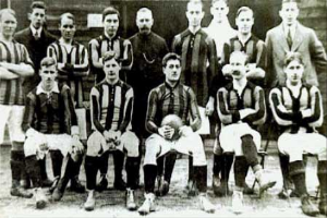 Ein Schwarz-Weiß-Foto einer Fussballmannschaft, mit einigen stehenden und einigen sitzenden Spielern vor einer Wand, mit dem Text "Ballymena Football Club" unten.