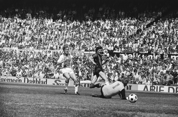 Schwarzes Foto von Männern, die auf einem Feld Füßball spielen, mit Zuschauern im Hintergrund und einer Bundesliga 1978-79 Ajax 1-1 Hannover 96 Fahne.