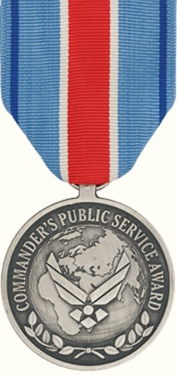 Eine silberne Medaille mit einer rot-weiß-blauen Schleife, beschriftet mit 'Commander's Public Service Award', vor einem weißen Hintergrund.