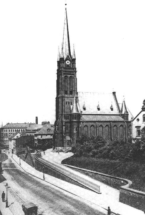 Schwarzes und weißes Foto einer Stadtstraße mit St. Peter Kirche im Hintergrund in Wiesbaden, Deutschland, gesäumt von Gebäuden, Bäumen, Fahrzeugen und einigen Fußgängern.