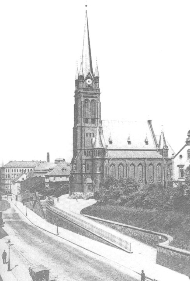 Schwarzes und weißes Foto einer Stadtstraße mit St. Peter Kirche im Hintergrund in Wiesbaden, Deutschland, gesäumt von Gebäuden, Bäumen, Fahrzeugen und einigen Fußgängern.
