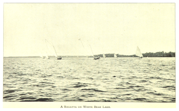 Regatta am Weißen Bärensee mit Booten auf dem Wasser, Bäumen im Hintergrund und Himmel darüber.
