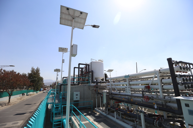 Großes industrielles Gebäude mit umfangreicher Rohrleitung, Solarmodulen auf dem Dach und Infrastruktur in der Umgebung, vor einem klaren blauen Himmel auf einem Hügel in Kalifornien.