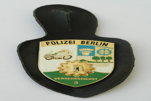 Ein Polizeistern mit der Aufschrift 'Polizei Berlin' auf einem blauen Hintergrund mit einem weißen Stern in der Mitte, umgeben von einem weißen Rand.