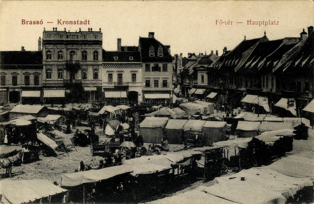 Schwarz-weiß-Foto eines vollen Marktes in Kronstadt, Deutschland, mit Menschen, Zelten und Gebäuden im Hintergrund.