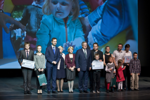 Eine Gruppe von Menschen auf einer Bühne mit Taschen und Urkunden, im Hintergrund ein Bildschirm mit einem Bild von einem Kind und anderen, was auf ein Wohltätigkeitsereignis hinweist.