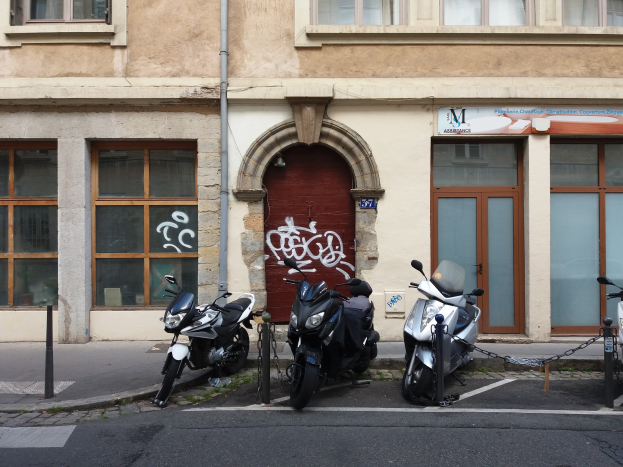 Drei Motorräder in einer Reihe vor einem Gebäude mit Graffiti an den Wänden, Fenstern, einer Tür und einer sichtbaren Leitung geparkt.