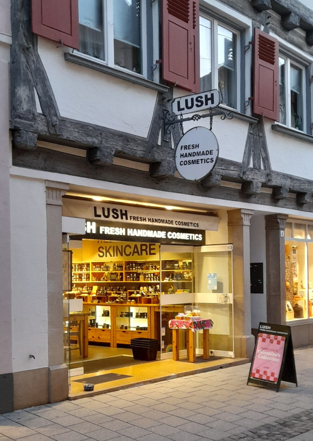 Vorderfront eines "Lush Skincare"-Ladens mit sichtbarer Innenausstattung, Schreibtisch, Stuhl und Bodenbelag.
