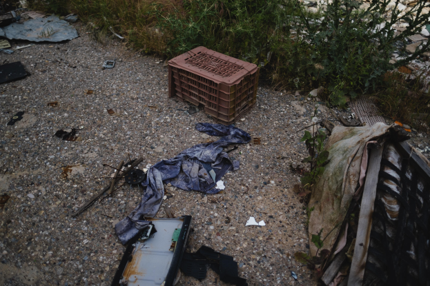 Müllhaufen einschließlich eines Plastikbehälters und Kleidung neben einer Straße nahe einem Zaun.