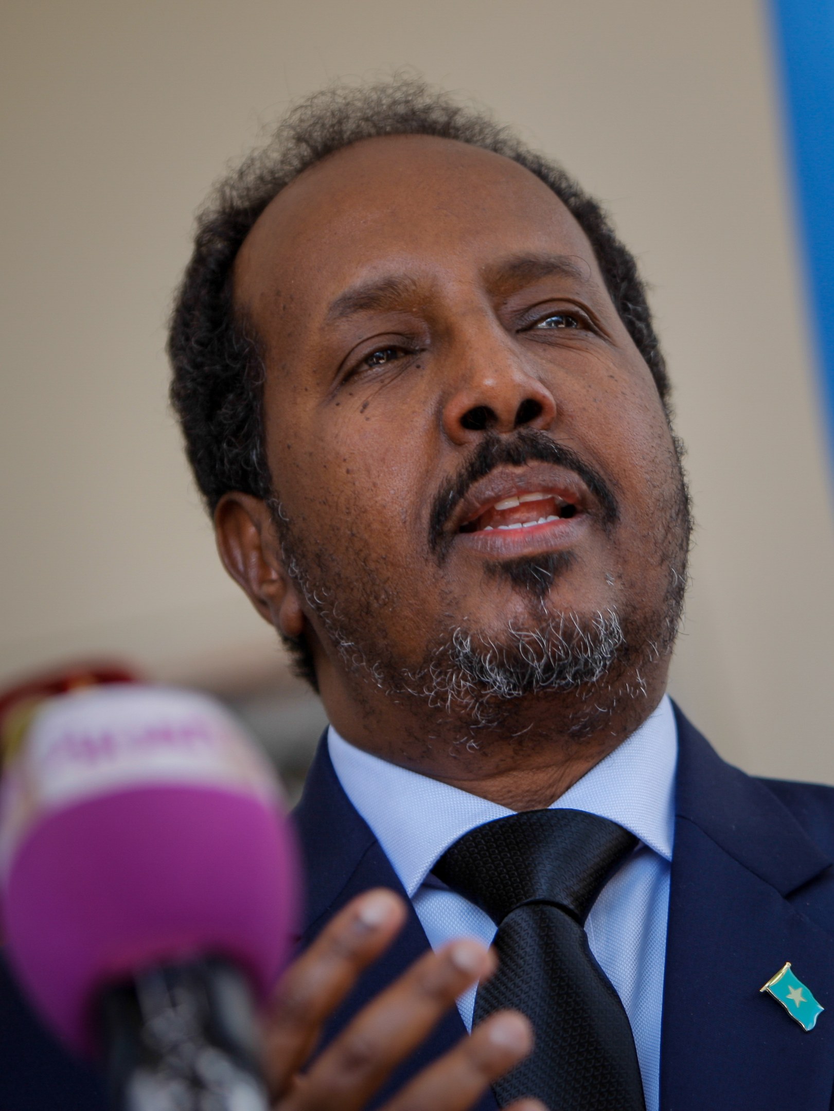 Ein Mann in Anzug und Krawatte, der in ein Mikrofon spricht, vor einem unscharfen Hintergrund.