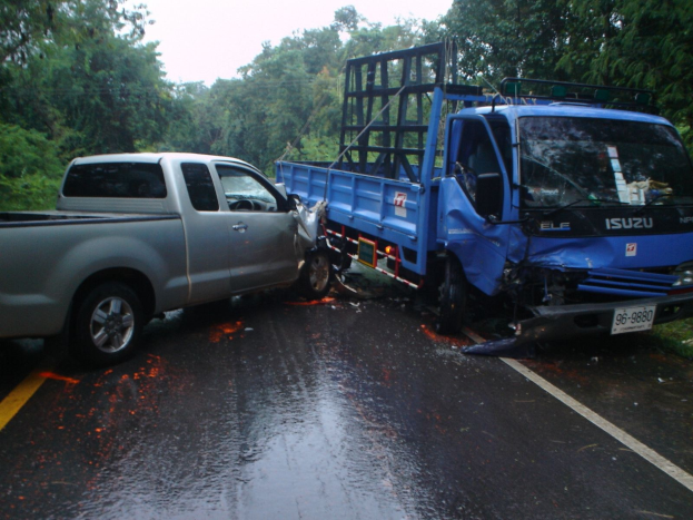Ein schwer beschädigtes LKW mit eingedrückter Front und verbeulter Karosserie am Straßenrand, umgeben von Bäumen unter einem klaren blauen Himmel.