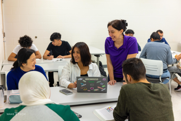 Eine Gruppe von Menschen in einem Klassenzimmer, die um einen Tisch sitzen und Laptops, Bücher und andere Gegenstände haben, die über Klimawandel diskutieren, wie es im Bildtitel angegeben ist.