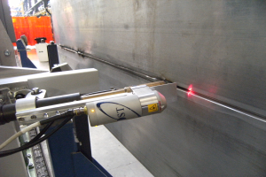 Heller Laserstrahl aus einer Schneidmaschine, der einen Fabrikarbeitsplatz beleuchtet, mit einer Wand auf der rechten Seite und Hintergrundobjekten.