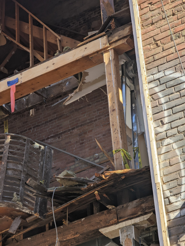 Teilweise abgerissenes Gebäude mit verstreuten Holzplanken und Trümmern, zerbrochene Fenster und Türen.