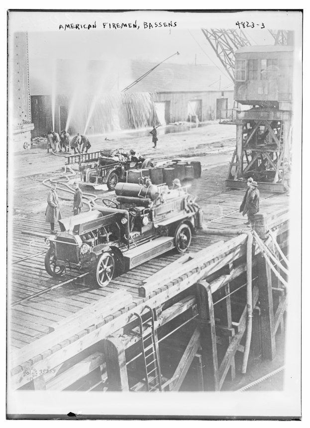 Ein Schwarz-Weiß-Foto eines Löschfahrzeugs auf einer Brücke mit einigen Menschen drumherum, eine Leiter führt hinauf zur Brücke, ein Gebäude im Hintergrund und Text oben auf dem Bild.