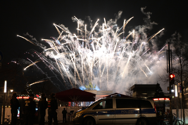 Polizeiauto vor einer Menschenmenge mit farbigen Feuerwerken im Hintergrund geparkt.