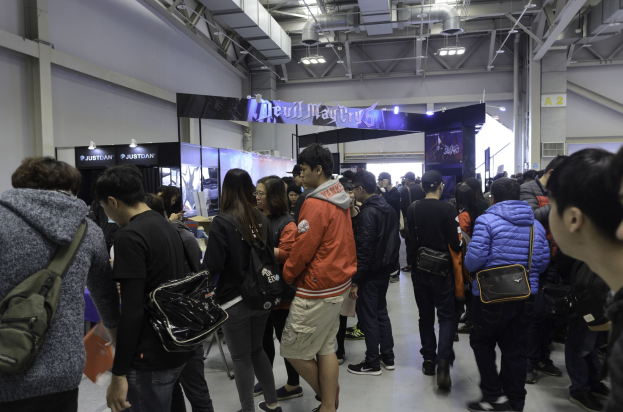 Gruppe von Menschen vor einer Menge an einer Gaming-Messe, mit Schildern, Lichtern und Rohren im Hintergrund.