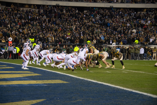 Ein Fuballspiel im Gange mit Spielern auf dem Boden in Sportbekleidung und Helmen, betrachtet von einem Stadionplatz.