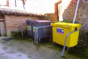 Zwei gelbe und graue Mülltonnen mit Rädern stehen nebeneinander vor einem Gebäude mit einer Wand und einem Fenster.