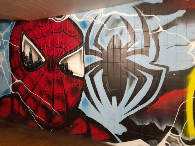 Buntes Wandgemälde von Spider-Man in rot und blau mit Webmuster und großem Spinnenlogo auf der Seite eines Gebäudes.