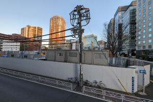 Eine Stadtstraße mit hohen Gebäuden, Strommasten, Fahrzeugen, Fahrrädern, Bäumen und einem klaren blauen Himmel.
