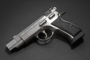 Eine Edelstahl-Smith & Wesson M&P Shield M2 0,9-mm-Halbautomatikpistole mit strukturiertem Griff und der Aufschrift "Spitfire", die auf einer schwarzen Oberfläche präsentiert wird.