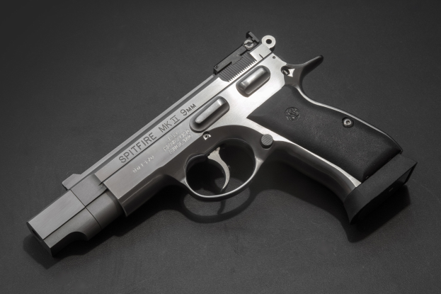Eine Edelstahl-Smith & Wesson M&P Shield M2 0,9-mm-Halbautomatikpistole mit strukturiertem Griff und der Aufschrift "Spitfire", die auf einer schwarzen Oberfläche präsentiert wird.