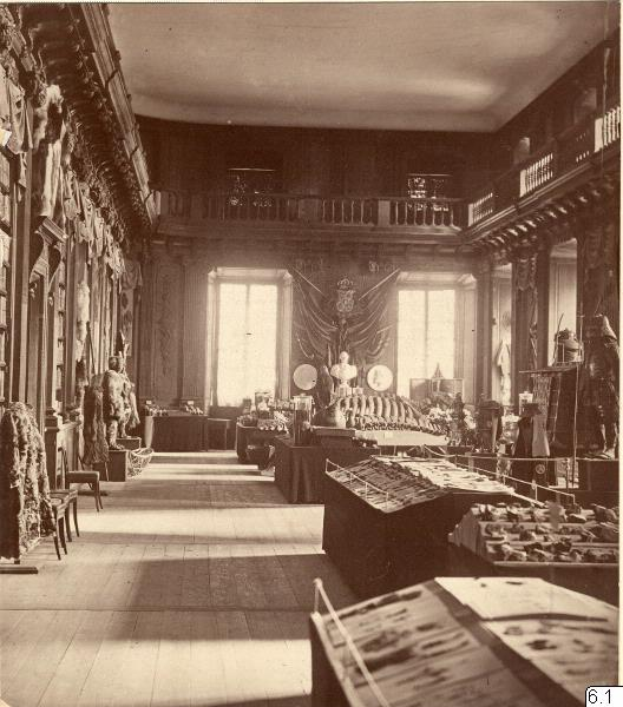 Ein altes Schwarz-Weiß-Foto eines Raums voller Tische, Stühle, Skulpturen an den Wänden, Fenstern, Vorhängen, Geländern und anderen Gegenständen mit der Aufschrift "The Museum of Fine Arts, London" unten.