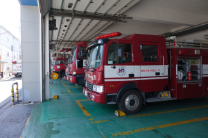 Feuerwehrfahrzeuge in einer Parkgarage geparkt mit einem Gebäude auf der linken Seite und anderen Fahrzeugen auf der rechten Seite, vor Gebäuden, Polen, Drähten und dem Himmel.