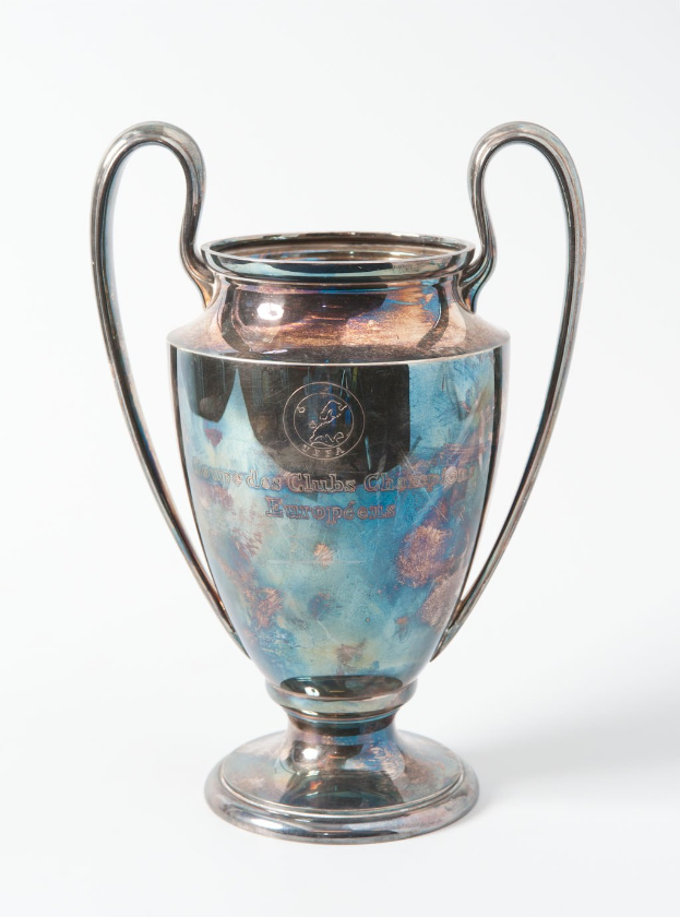 UEFA Champions League-Trophäe, ein silberner und blauer Stahlpokal mit zwei Griffen, der mit "UEFA Champions League" beschriftet ist, vor einem weißen Hintergrund dargestellt.