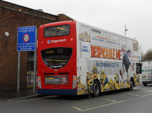 Weißer und roter Bus auf einer Straße mit einer roten Backsteinmauer und einem blauen Warnschild im Hintergrund.