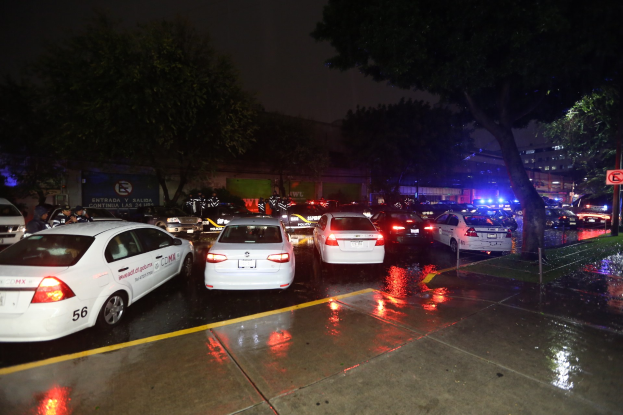 Polizeifahrzeuge auf einem Parkplatz bei Nacht mit einem Schild, Bäumen, Gebäuden, einer Fahne und einem bewölkten Himmel.