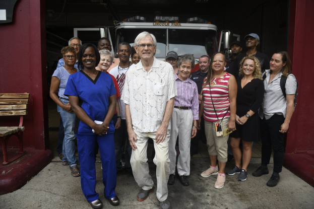 Eine Gruppe von Freiwilligen vor einem Feuerwehren, mit einer Bank links und einer Wand im Hintergrund.