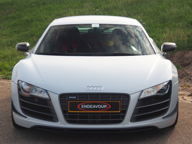 Ein weißer Audi R8 parkt am Straßenrand, umgeben von saftigem Grün.