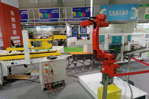 Roboter sitzen auf einem Tisch in einer Fabrikumgebung umgeben von Maschinen, Kabeln, beschrifteten Leiterplatten und beleuchteten Komponenten, mit Menschen im Hintergrund.