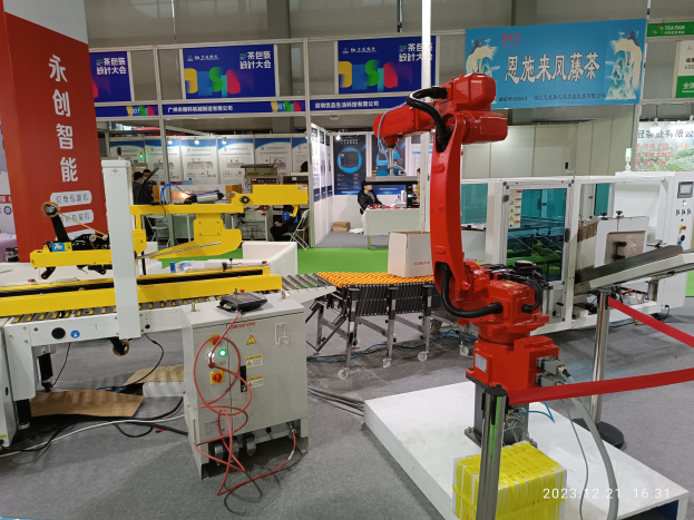 Roboter sitzen auf einem Tisch in einer Fabrikumgebung umgeben von Maschinen, Kabeln, beschrifteten Leiterplatten und beleuchteten Komponenten, mit Menschen im Hintergrund.