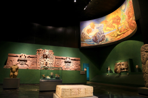 Ausstellung verschiedener Artefakte im Mexiko-Stadt-Museum der Anthropologie, darunter Skulpturen, Tischobjekte, eine Texttafel, eine Wandmalerei und Deckenleuchten.
