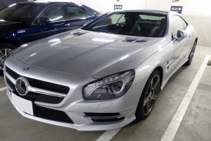 Silberner Mercedes-Benz SL-Class in einer Parkgarage neben anderen Autos geparkt, mit sichtbaren Garagenwänden und Texttafeln im Hintergrund.