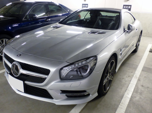Silberner Mercedes-Benz SL-Class in einer Parkgarage neben anderen Autos geparkt, mit sichtbaren Garagenwänden und Texttafeln im Hintergrund.